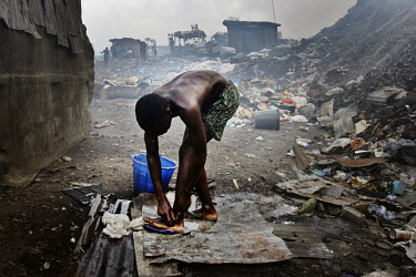 A scavenger who lives at the Olusosun garbage landfill bathes outdoors. The Olusosun dump is Nigeria's largest trash heap comprising over 100 acres of garbage and is believed to be the largest in Afri...