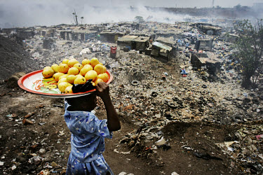A girl carrying fruit on her head descends on a village at the Olusosun landfill site. The Olusosun dump is Nigeria's largest trash heap comprising over 100 acres of garbage and is believed to be the...