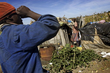 Unemployed and desperate, people scavenge through waste at a rubbish dump looking for items to sell. A squatter camp has been built up, its huts constructed out of plastic sheeting and other scavenged...