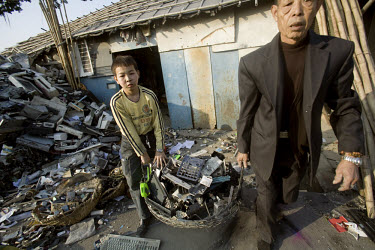 A young boy and an old man carrying a basket of electronic trash outside an e-waste recycling workshop. Every year Guangdong receives more than a million tons of computer waste from countries all over...