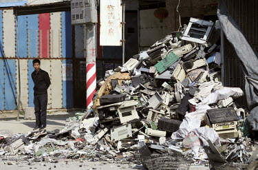 A man stands next to a large heap of electronic trash scattered by the side of the road. Every year Guangdong receives more than a million tons of computer waste from countries all over the world. Abo...