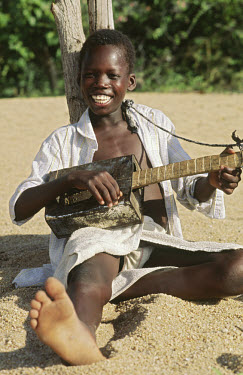 A smiling boy playing a guitar made from an oil can.