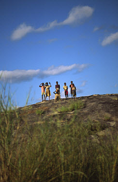 Children waving from a high rock above a rural road.