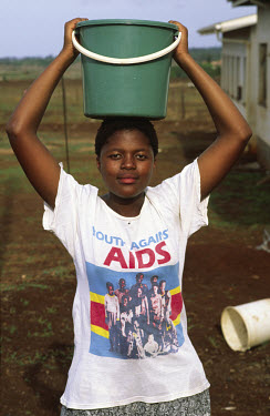 A girl wearing a 'Youth Against Aids' T-shirt carries a bucket of water.