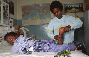 A mother helps her disabled son practise physiotherapy exercises at a polio clinic.