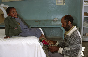 A father adjusting his son's orthopaedic leg brace (calipers) at a polio clinic.
