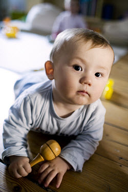 A 10-month-old baby boy playing with a rattle near his twin at home.