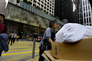 A rubbish collector (freelance recycling) pushing a cart loaded with cardboard past a freshly refurbished Louis Vuitton (LVMH) store in the Central District.