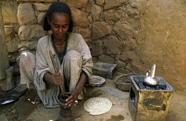 A woman grinding roasted coffee beans using traditional methods before brewing a pot of coffee.