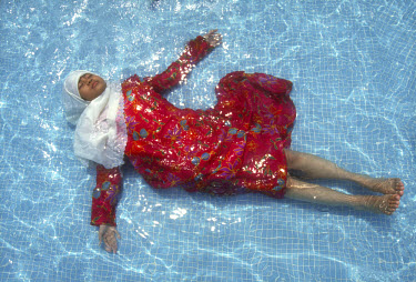 A young Muslim girl relaxing in a public swimming pool below the Petronas Towers.