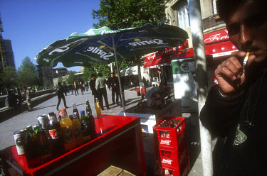 A street vendor selling bottles of Coca Cola, Fanta and Sprite smokes a cigarette by his soft drink stall.