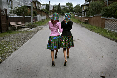 Two village girls dressed up in traditional clothes and modern high heels walking through the streets of Budesti.