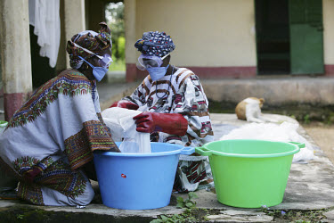 Women soaking mosquito nets in insecticide. They are taking correct safety precautions by wearing rubber gloves and eye goggles.