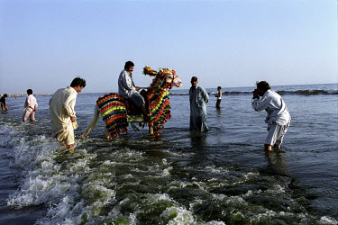 Labourers enjoy a break from work at the Gaddani ship-breaking yard by playing in the surf with a brightly decorated horse.