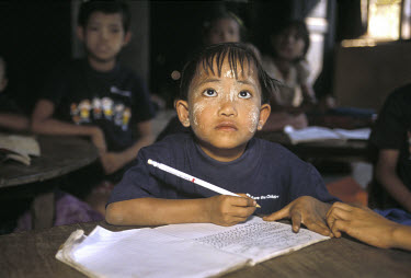 A child with 'tanaka' on his face studies in a rural classroom. Tanaka is a natural sun-block made from the bark and wood of a tanaka tree.