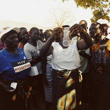 A woman from the organisation OMES demonstrates to a group of people how to use a condom. OMES (Women's AIDS Education Organization) is an organisation of women who educate people on HIV/AIDS. They wo...