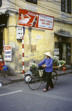 A woman selling flowers from her bicycle walks under a Coca-Cola advert.