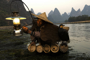 A cormorant fisherman lights his paraffin lamp ready for some night fishing on the Li River with his cormorants. The cormorants dive into the river from his bamboo raft and grab the fish in their beak...