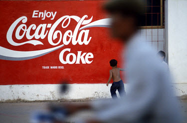 Children play in front of a Coca-Cola advert painted on a city wall.