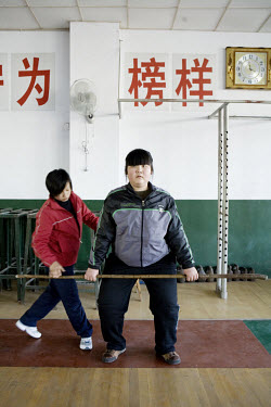 A new student being coached at weight-lifting at the Weifang City Sports School, one of 3,000 state-run athletic academies that consign nearly 400,000 youngsters to a form of athletic servitude. In th...