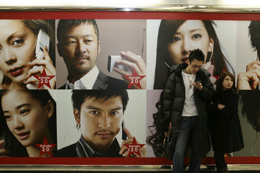 A young man checks his mobile phone in front of a large advertisement for DoCoMo telecommunications company along the underground concourse within Shinjuku Station. JR (Japan Railways) has 16 tracks a...