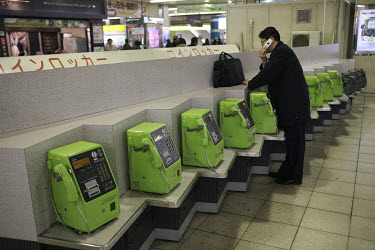 A businessman uses his mobile while standing next to a row of public telephones in Shinjuku Station. Public telephone use in Tokyo, like in other cities around the world, has fallen dramatically since...