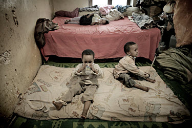 Three year old twins Hassan and Hossin (sitting on the mattress on the floor) and their two year old sister Hannan, sit tied for six hours a day waiting for their mother to return. ^I have to tie them...