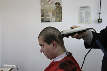 Conscript Kamil Wozniak has his head shaved, under a poster advertising the new, voluntary Polish army. This year's class of drafted recruits is the final one after 90 years of compulsory military ser...