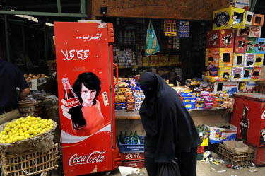 Covered woman passing a stall selling Coca-Cola in a market in Islamic Cairo.