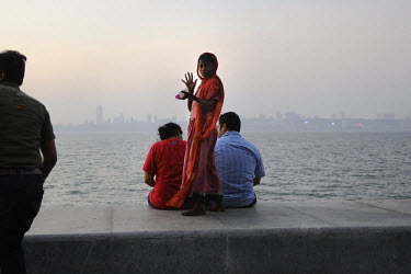 Girl beggar on the Marine Drive waterfront by a middle class couple enjoying the dusk.