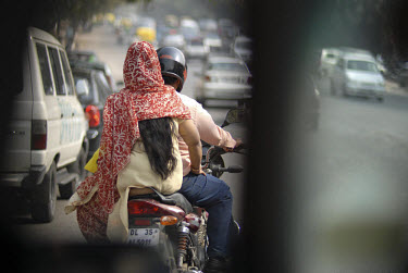 Woman riding side-saddle on the back of a motorbike through heavy traffic in central Delhi.