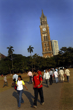 People walk through a park with a colonial-era clock tower and the Stock Exchange tower in the distance.