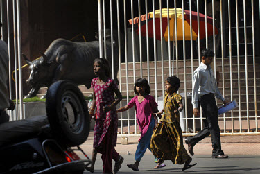 Street children running in front of a statue of a bronze bull at the fortified entrance to the Stock Exchange.