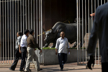 Investors and members of the public pass the statue of bronze bull at the fortified entrance to the Stock Exchange.