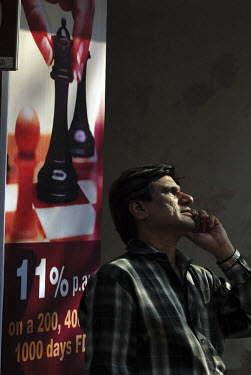 An investor talks on his mobile phone as he watches announcements as they come up on the outside of the Bombay Stock Exchange. Behind him an advert for a high interest deposit account tempts people to...