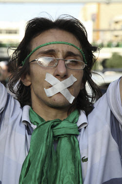A man in Haftetir Square wearing green, the colour of the opposition, and tape over his mouth as a symbol of his silent protest. Following a disputed election result, thousands of supporters of opposi...