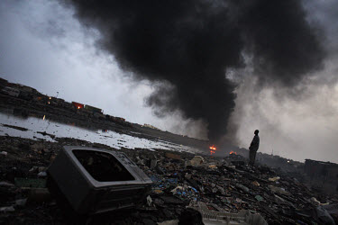 E-waste litters the ground while a huge fire burns at Agbogbloshie dump, which has become a dumping ground for computers and electronic waste from all over the developed world. Hundreds of tons of e-w...