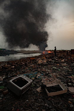 E-waste litters the ground while a huge fire burns at Agbogbloshie dump, which has become a dumping ground for computers and electronic waste from all over the developed world. Hundreds of tons of e-w...