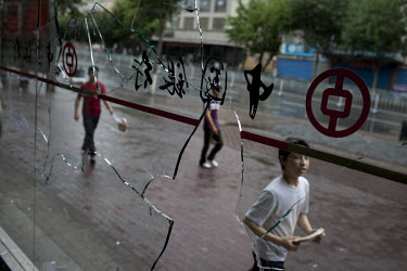 Uighurs pass a Bank of China window that was smashed during riots in the Uighur district of Urumqi. Ethnic violence between the Uighur and Han Chinese people had erupted in the city a few days earlier...