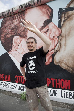 Russian artist Dmitry Vrubel standing in front of his famous Berlin Wall painting of Soviet leader Leonid Brezhnev kissing East German leader Erich Honecker. First painted in 1990, Vrubel, shown here...