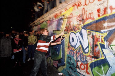 A man attacks the Berlin Wall with a pickaxe on the night of November 9th, 1989 as news spread rapidly that the East German Government would now start granting exit visas to anyone who wanted to go to...