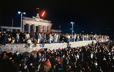 The Berlin Wall in front of the Brandenburg Gate on the night of November 9th, 1989. Thousands climbed on the Wall as news spread rapidly that the East German Government would now start granting exit...