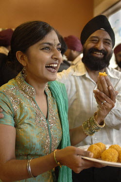Young British Indian woman eating laddoo at a Sikh social function in Leicester.