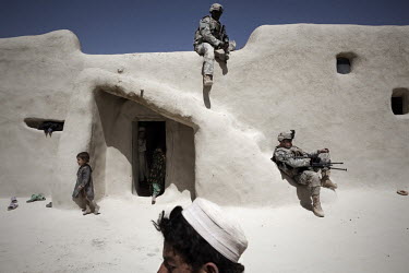 US Army soldiers from 1st Platoon, Baker Company, 3rd Battalion, 509th Infantry Airborne rest as an Afghan boy looks on while a compound is raided during an air assault operation to search for an IED...