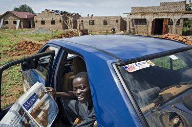 Son of businessman Nicholas Rajullah in a Mercedes reading financial news, in the background his father's construction project, the first hotel in Kogelo. On the car window is a sticker of Barack Obam...
