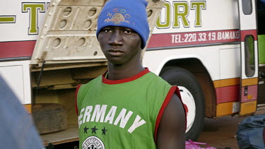 A migrant waits at the bus station in Bamako wearing a Germany football shirt. Many migrants travel to Europe with the dream to start a football career with a European club.