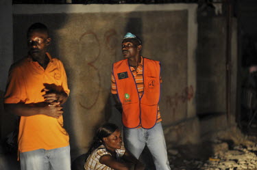 Three people sit beside the road in front of their destroyed houses as night falls in Port-au-Prince one week after an earthquake hit the country. The man on the right is wearing an Oxfam vest.A 7.0 m...