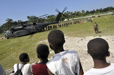 Children look on as US Marines of the 22nd Marine Expeditionary Force unload food aid from a navy helicopter south west of Leogane twelve days after an earthquake hit the country. A 7.0 magnitude eart...