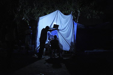 A man pushes a child in a wheelchair into a makeshift clinic in a dark park in the city centre. The clinic is run by medical students with the little medecine they could gather. Thousands of people ha...