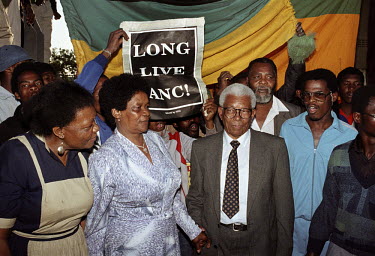 Walter Sisulu (right centre) of the African National Congress (ANC) with his wife Albertina after his release from prison. He had just arrived back in Soweto. Behind them a person holds up a poster wh...